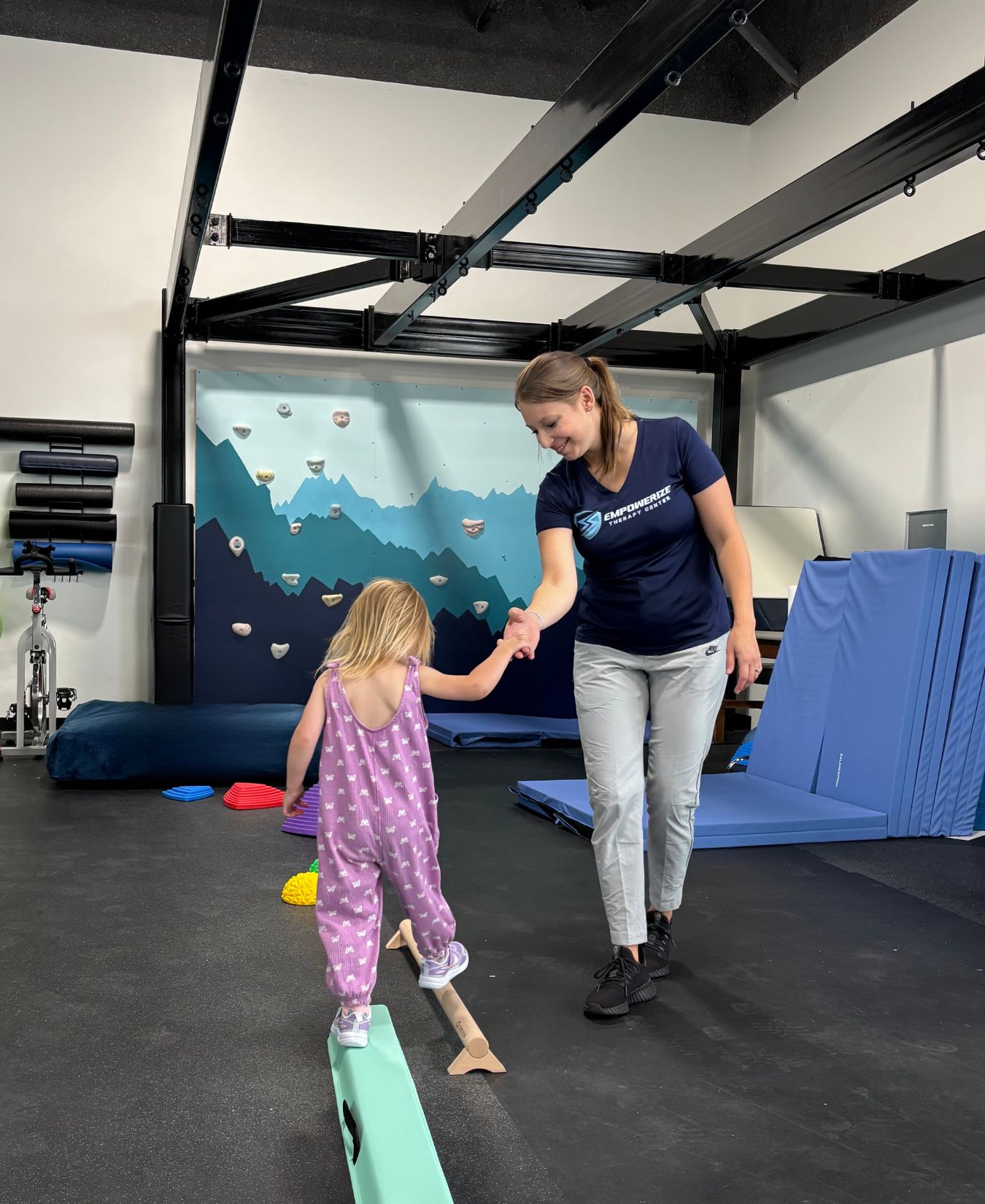 Child walking a balance beam holding a therapist’s hand