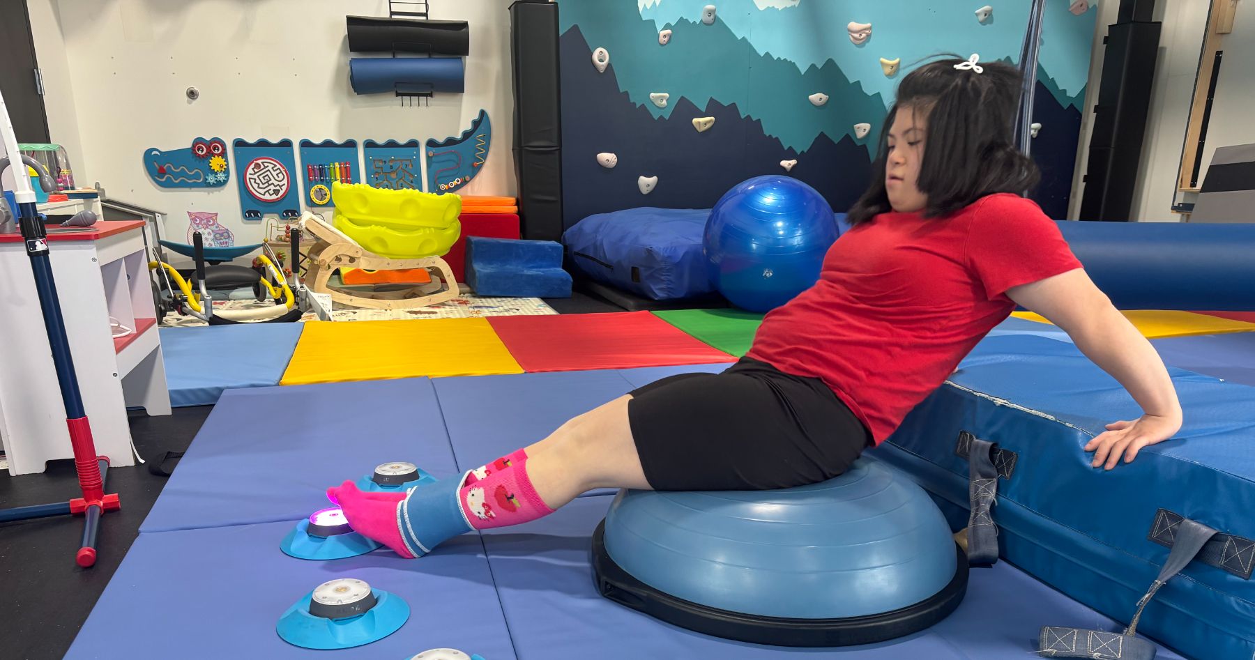 A child balances on a half-dome ball on the therapy gym mat