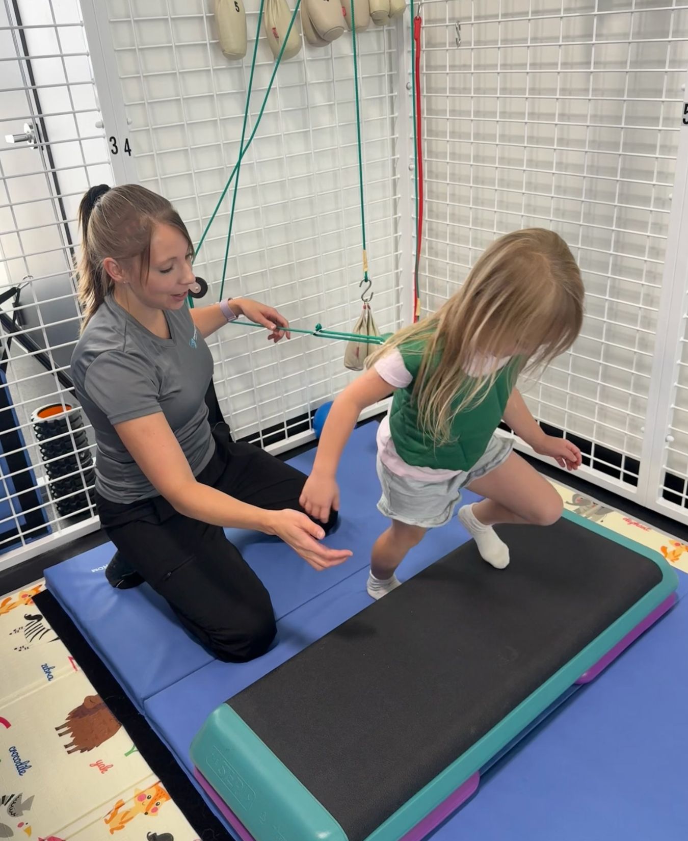 Child stepping up onto a platform with a therapist’s support